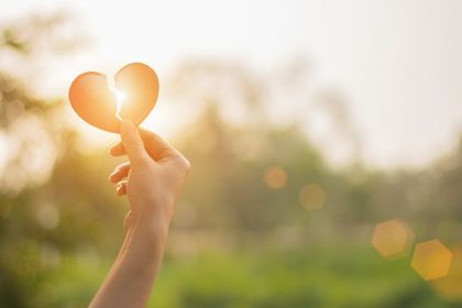 Hand holding a glowing heart shape against a warm, sunlit bokeh background