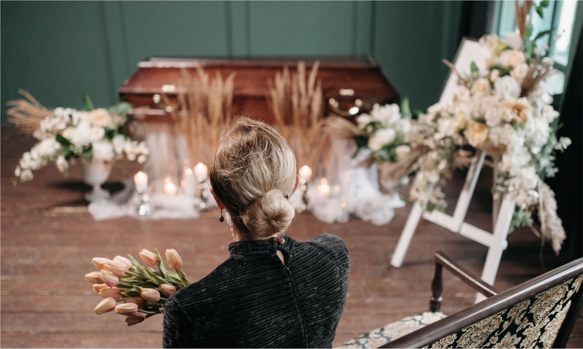 Person holding flowers at a funeral beside a casket and white floral arrangements