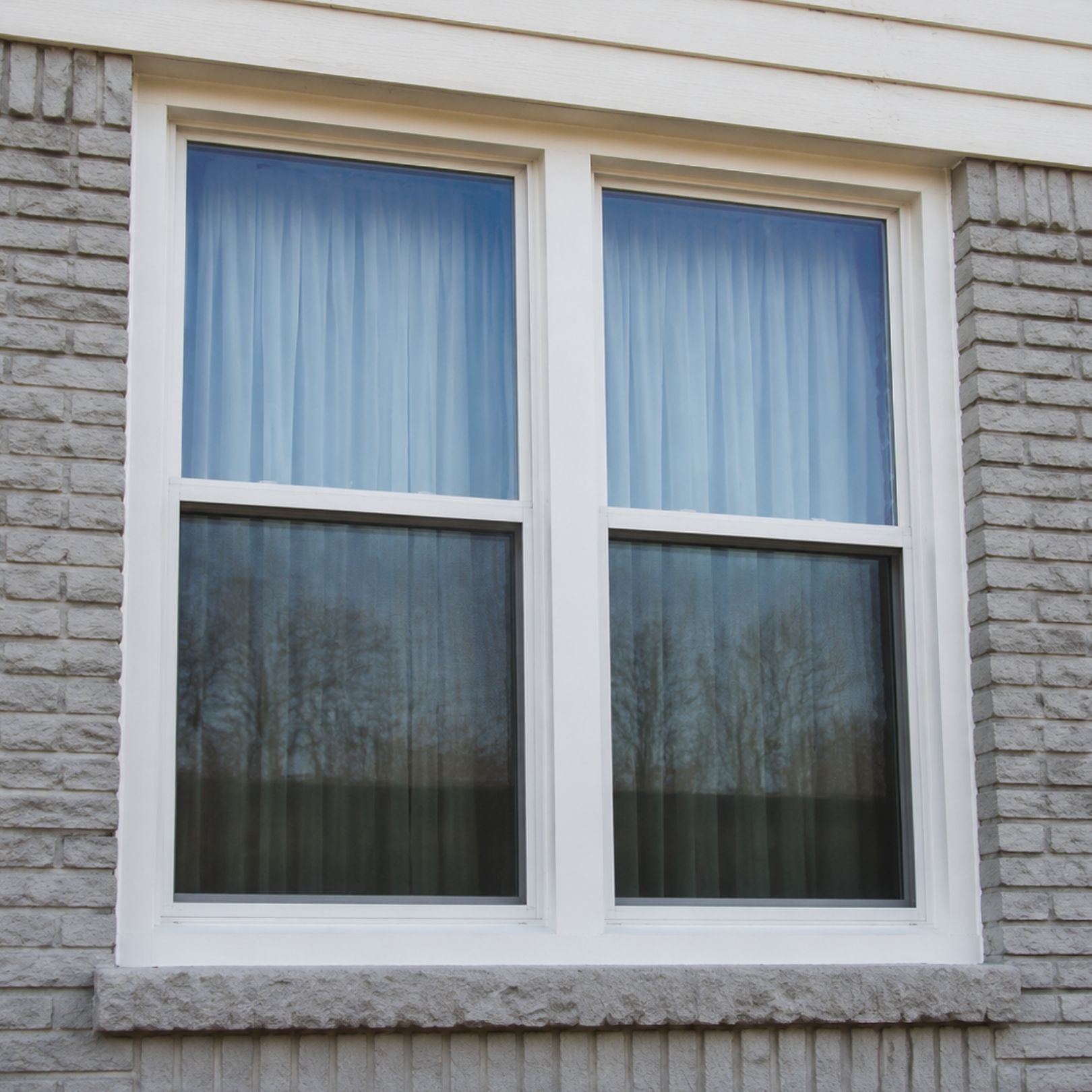 White-framed double window with curtains on a light stone exterior wall
