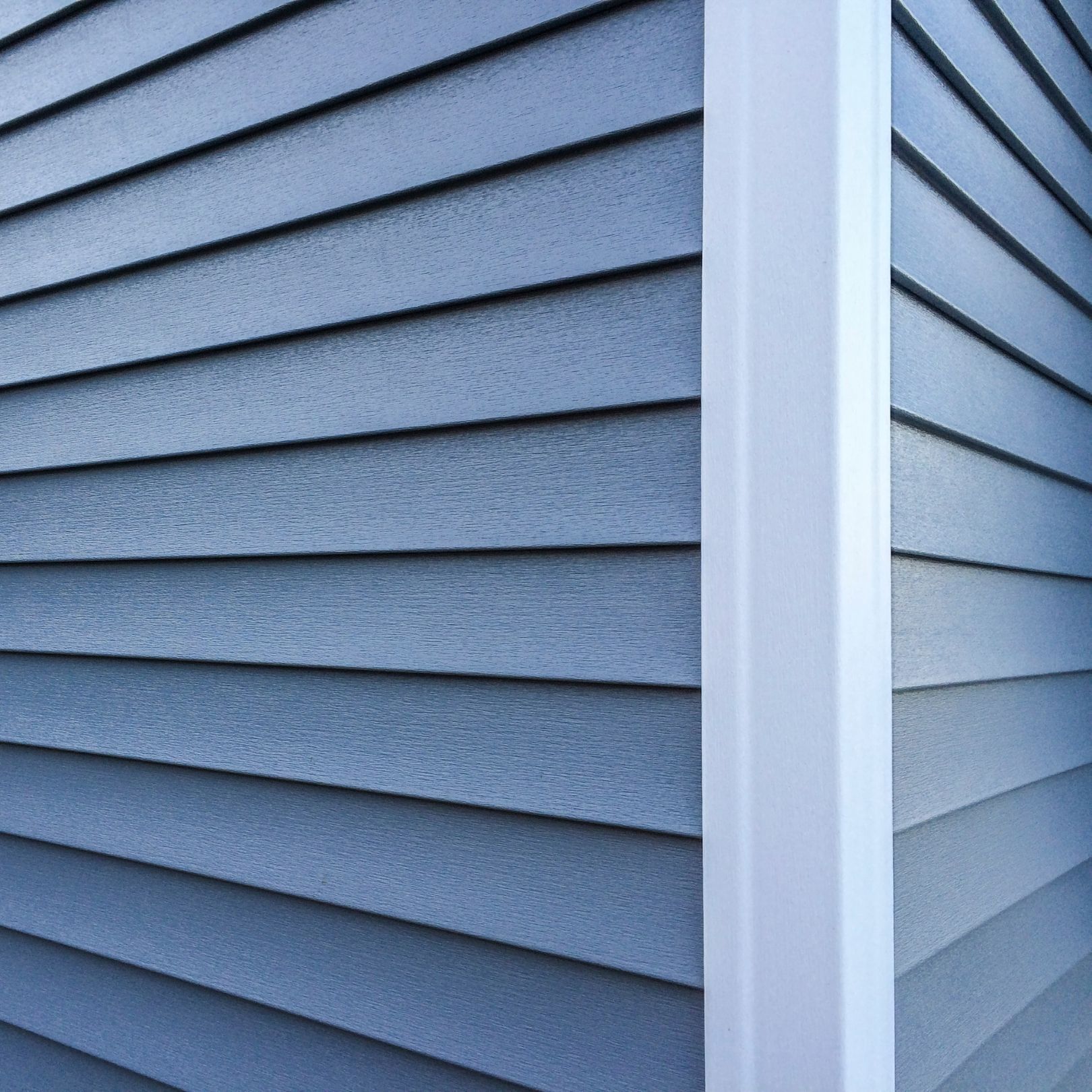 Close-up of blue-gray vinyl siding meeting at a building corner with white trim