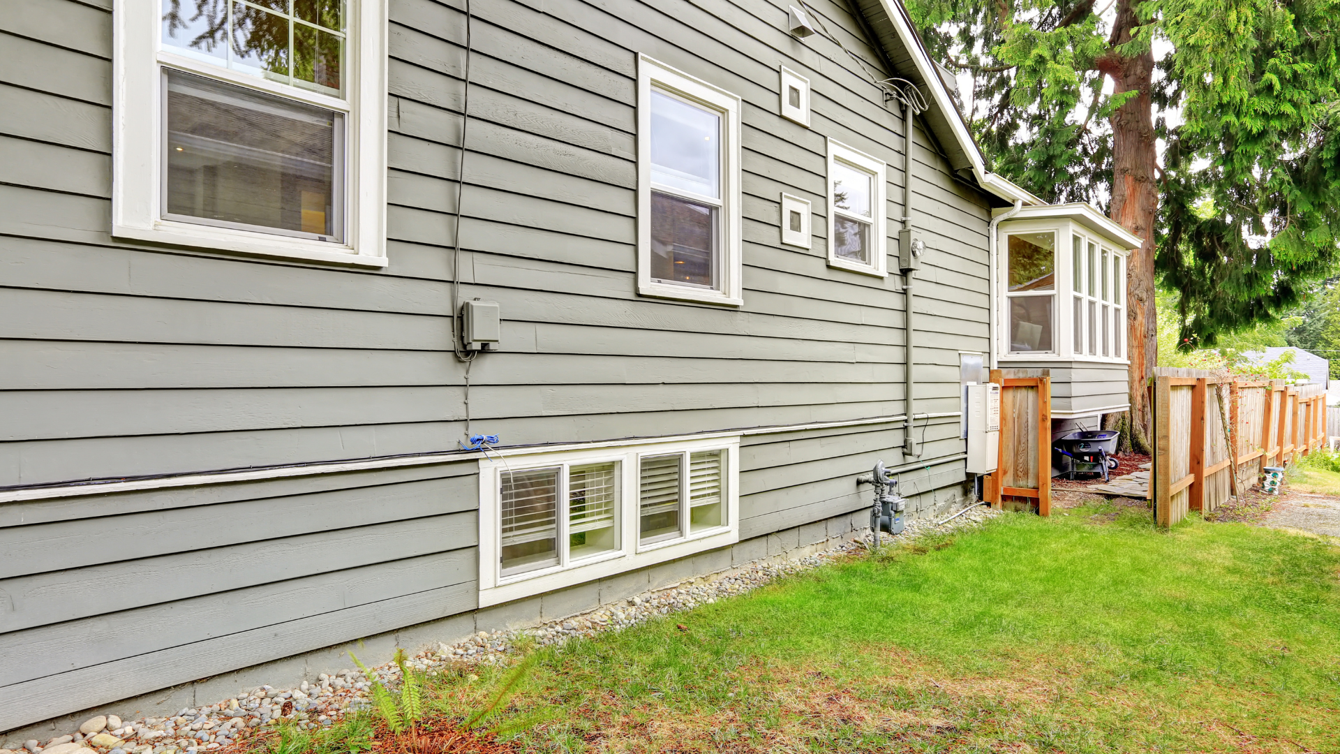 Garden hose spraying water on beige house siding beside a window