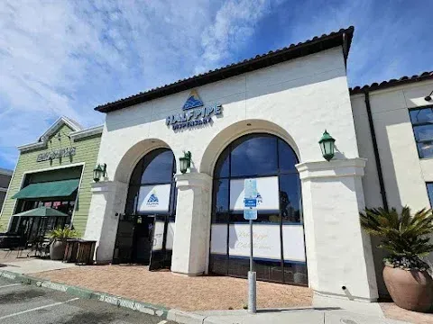 White stucco building with arched entrance and blue windows under a tiled roof