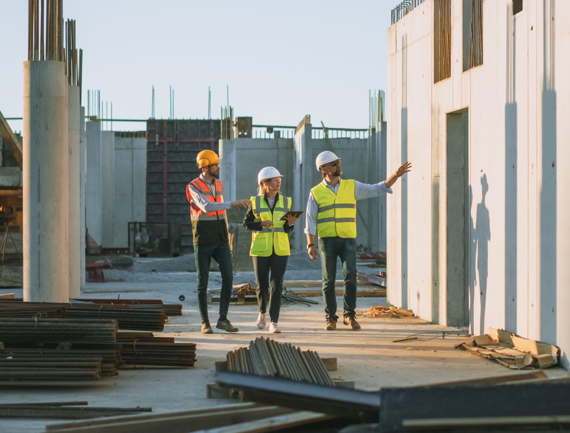 Three construction workers in safety vests and hard hats discussing plans at a building site.
