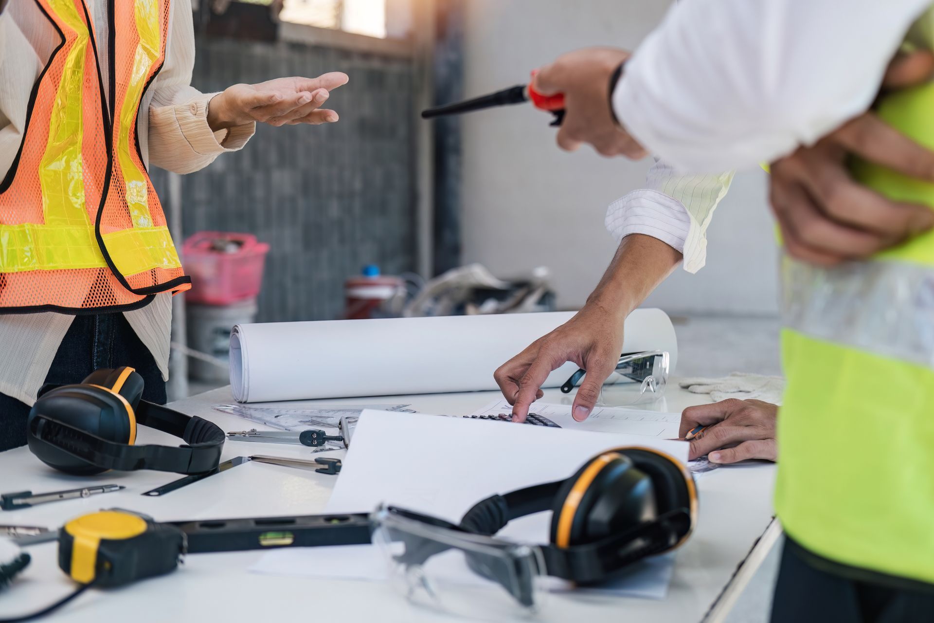 Construction workers reviewing plans at a table with tools, hard hats, and safety vests