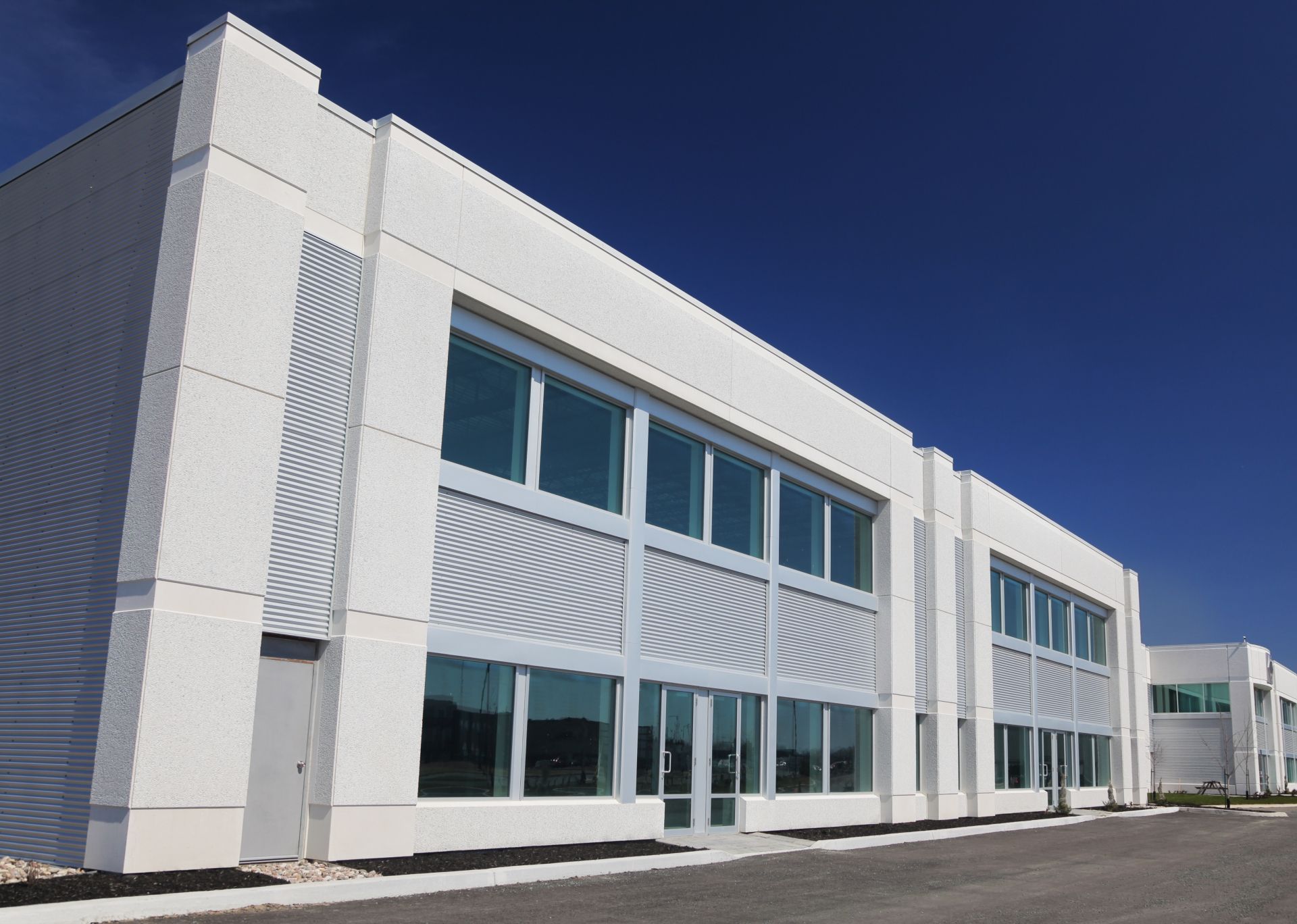 Modern white commercial building with large windows under a clear blue sky