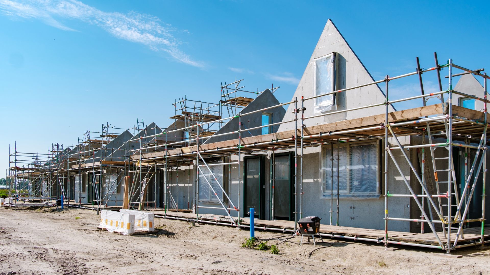 Row of newly built houses under construction with scaffolding and blue sky