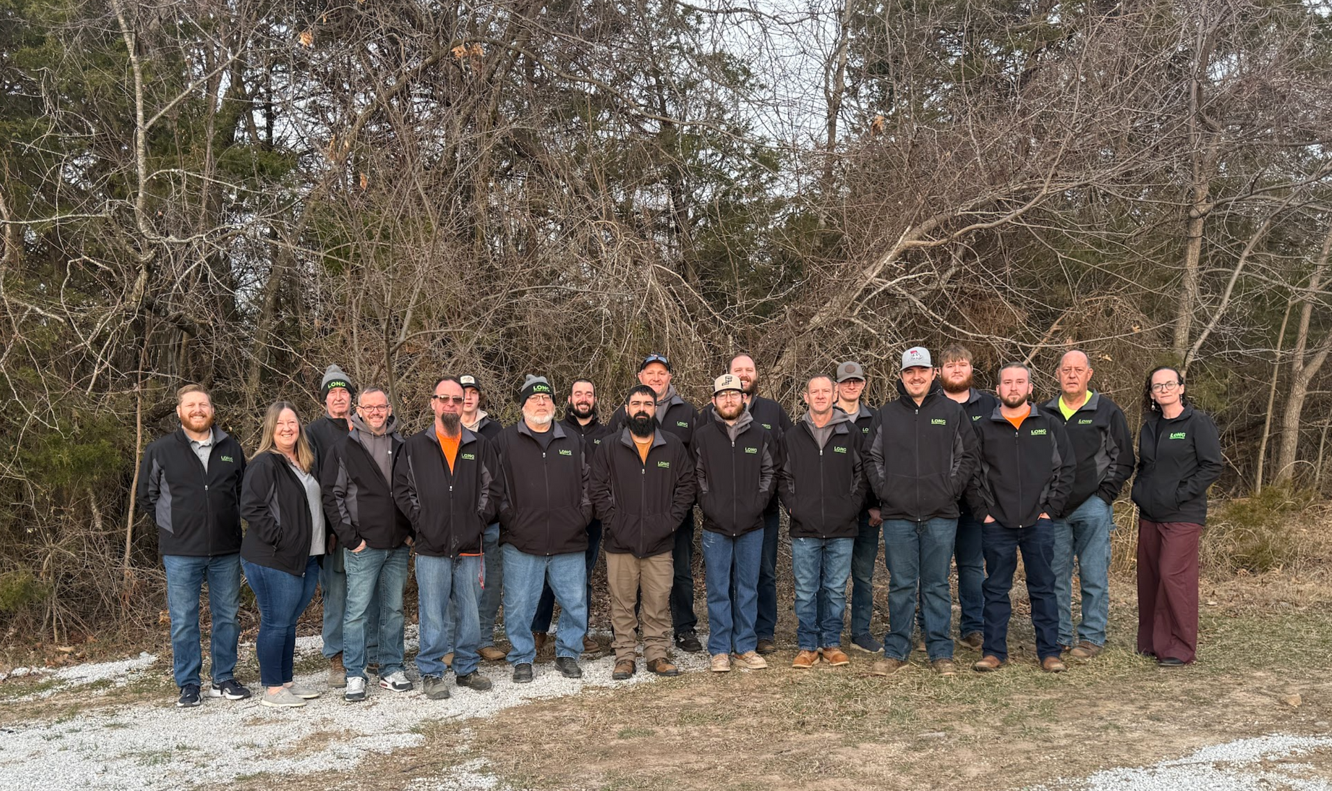 Group of people standing outdoors in winter jackets in front of leafless trees and snow-covered ground