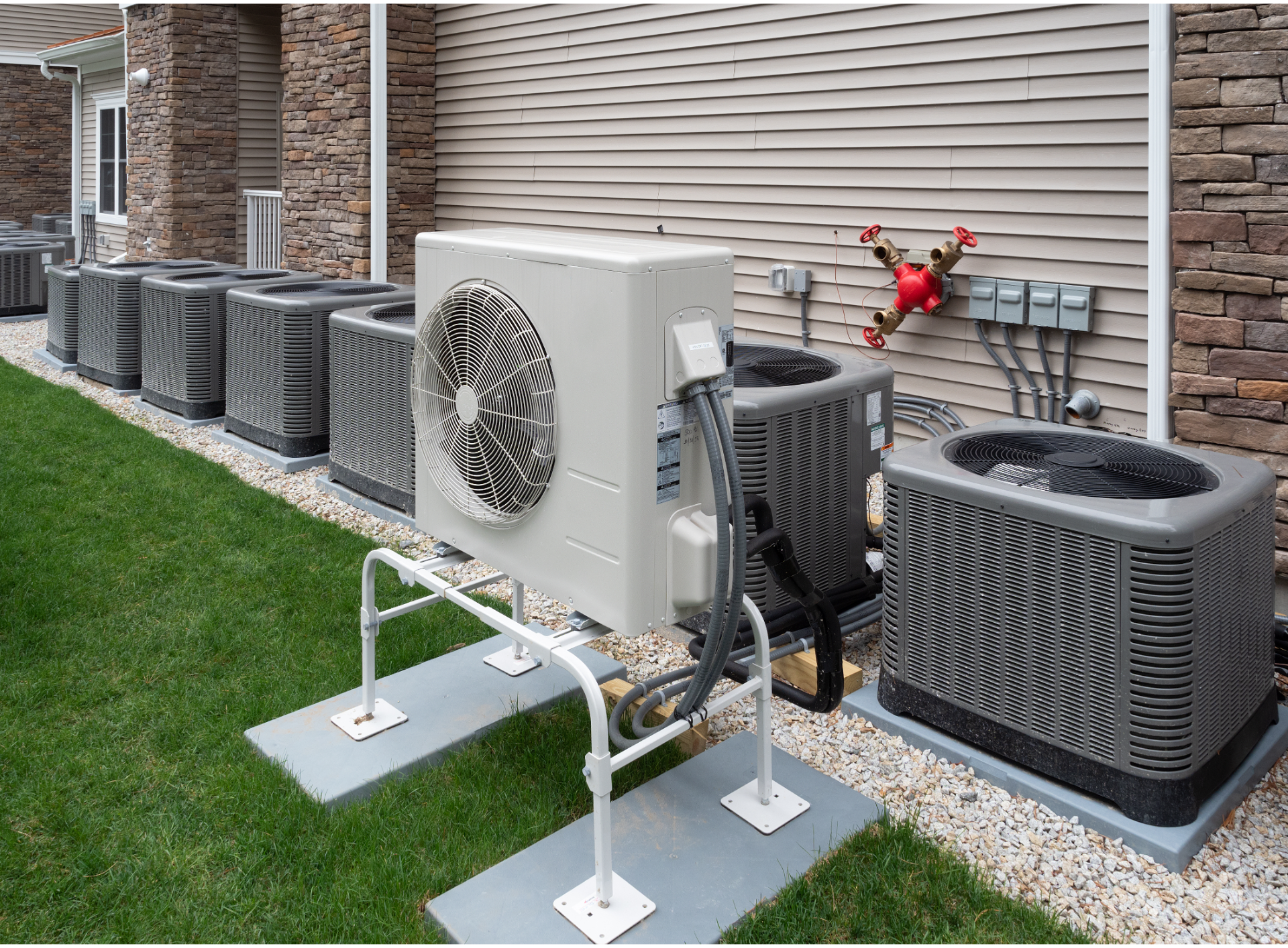 Outdoor HVAC units beside a house, with one white condenser mounted on a stand in the foreground.