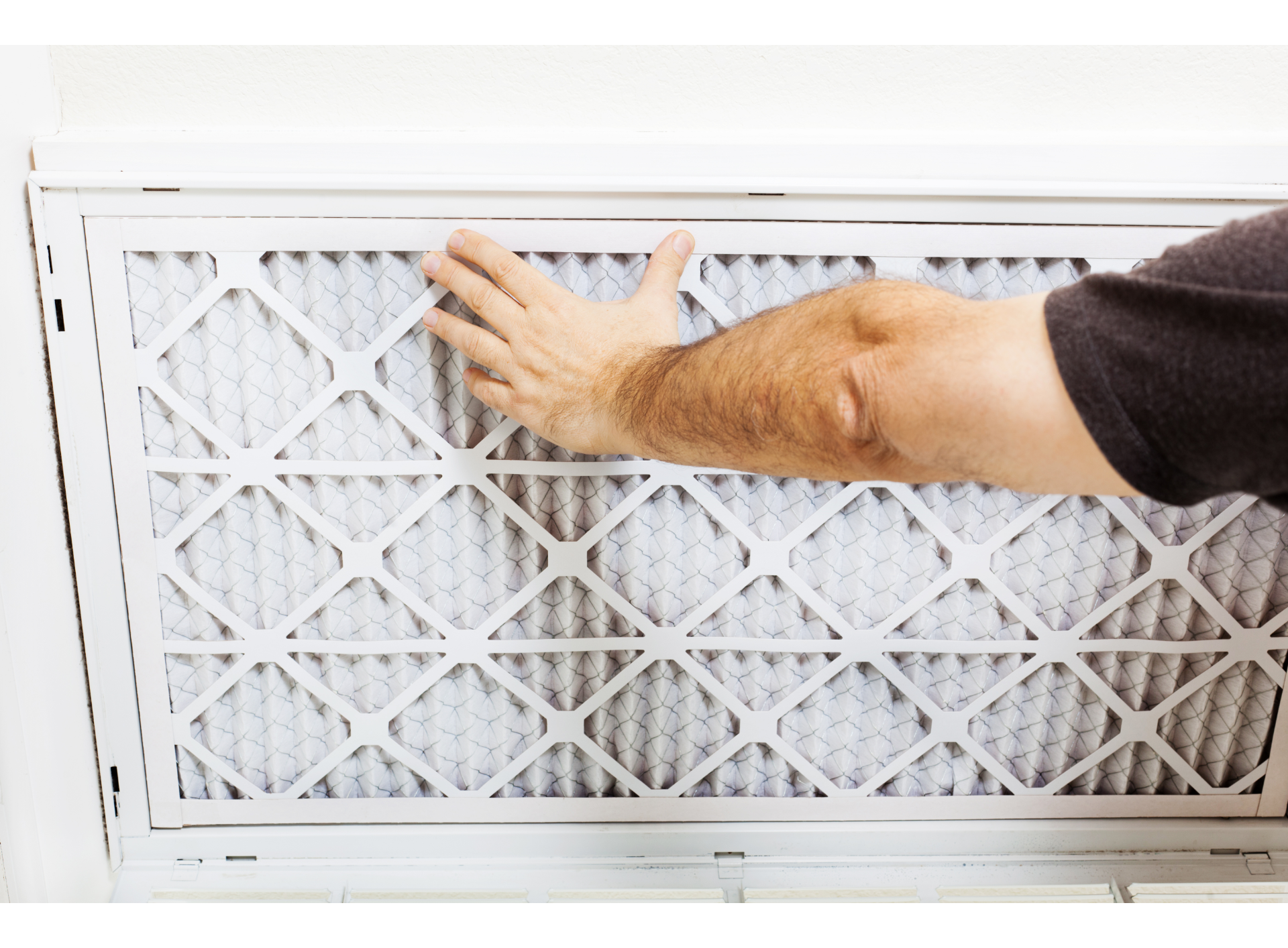 Hand replacing a white furnace air filter in a wall vent grille
