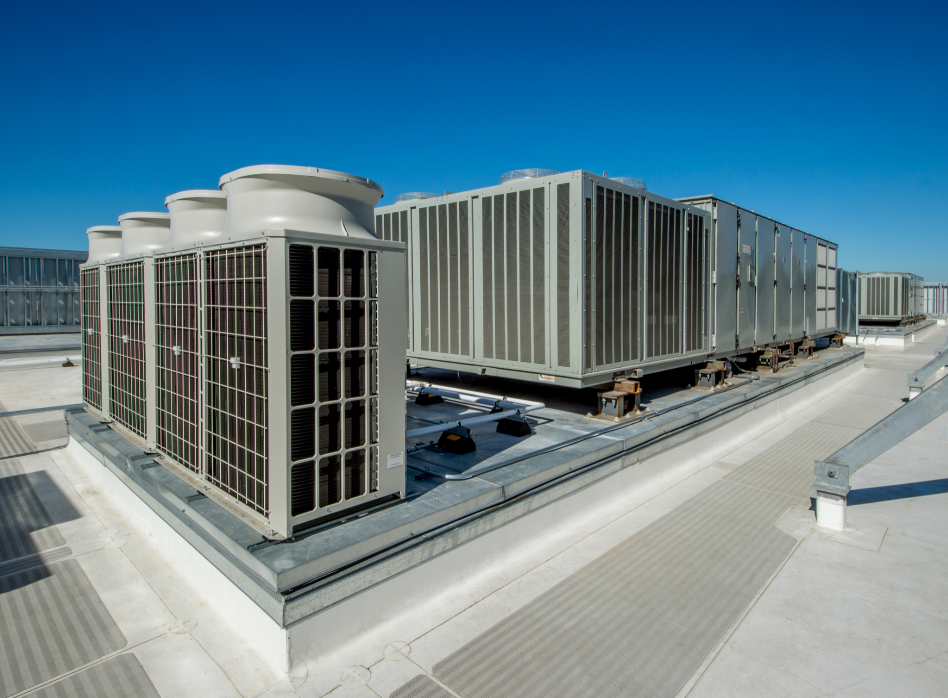 Rooftop HVAC units and cooling towers on a large industrial building under a clear blue sky