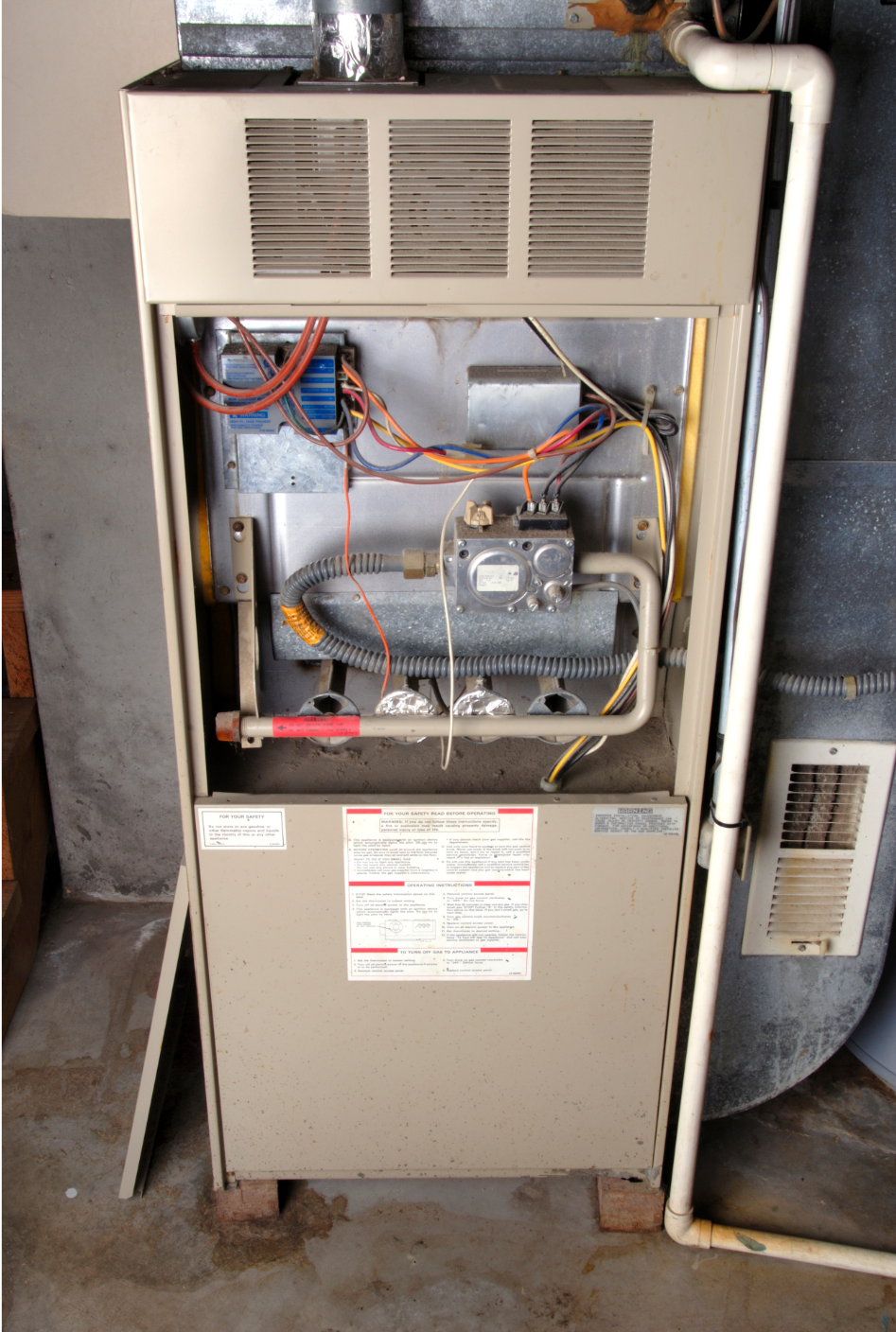 Open furnace with exposed wiring and ductwork in a utility room.