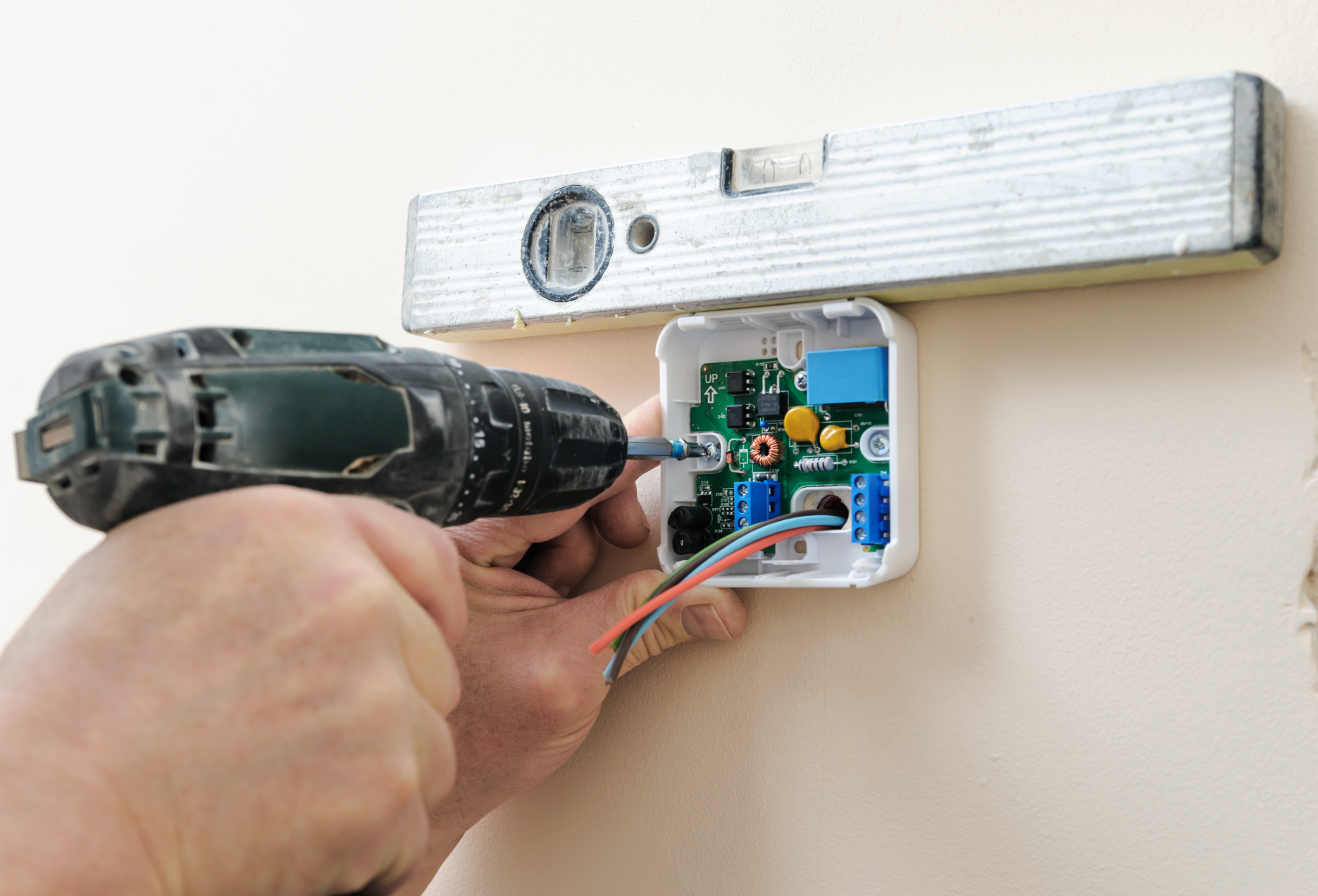 Hand drilling a wall-mounted electrical box under a level tool