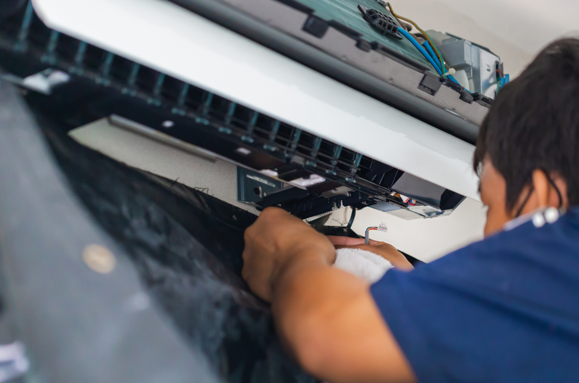 Technician repairing wiring inside a wall-mounted device, wearing a blue shirt.