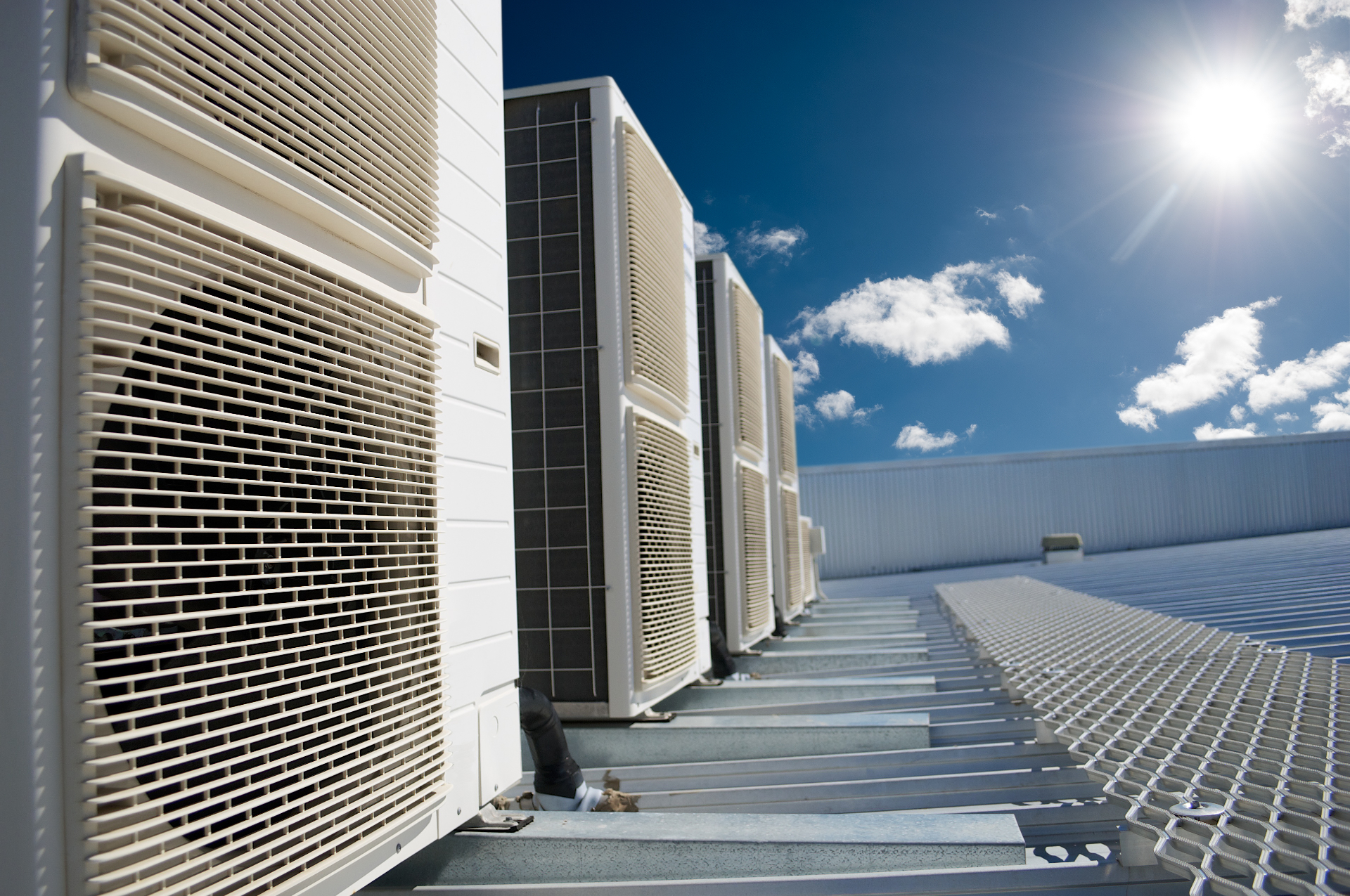 Row of outdoor air conditioning units on a sunny rooftop under a blue sky