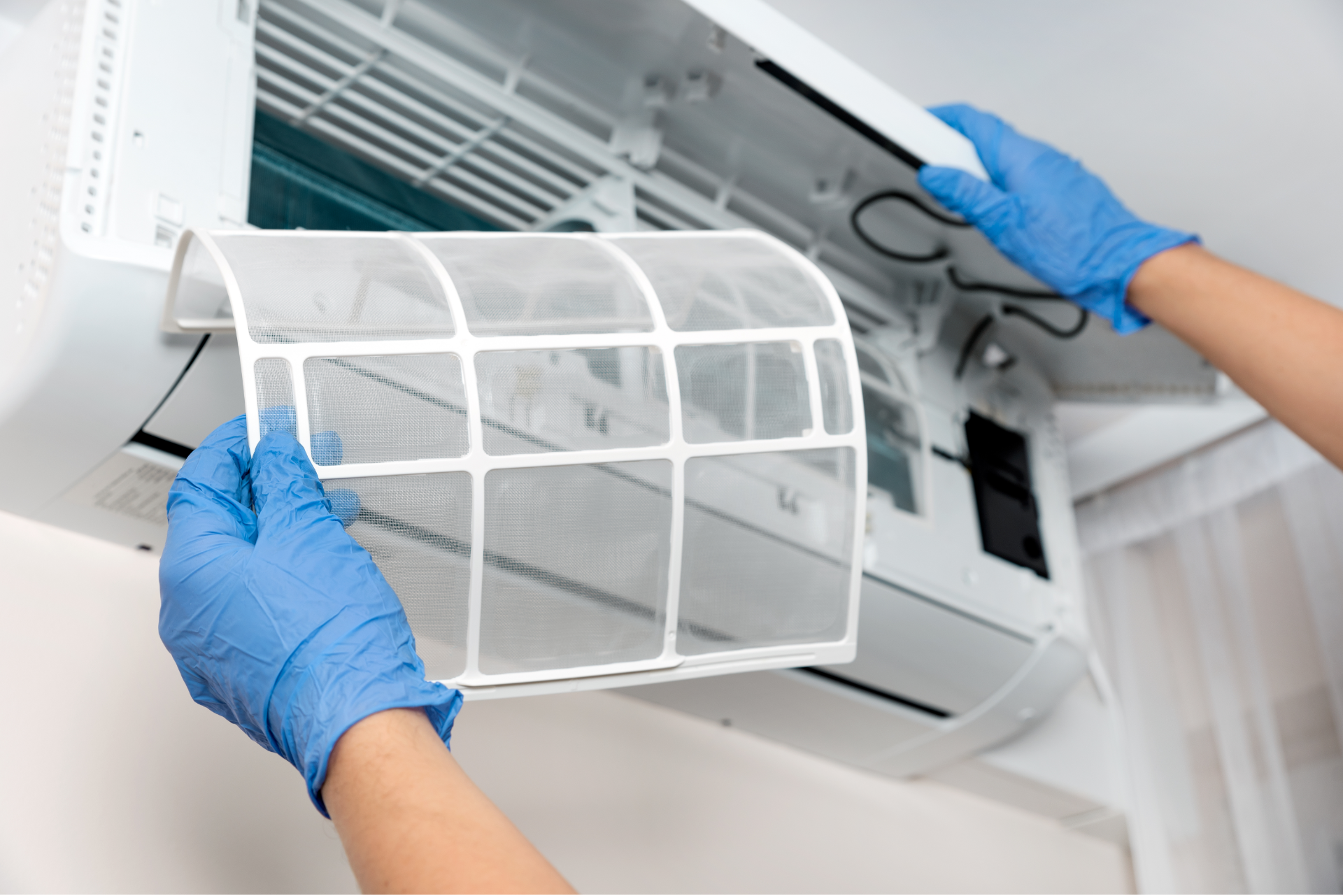 Gloved hands cleaning a wall-mounted air conditioner filter indoors