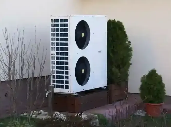 Outdoor air conditioning unit beside a building, next to shrubs and a leafless bush.