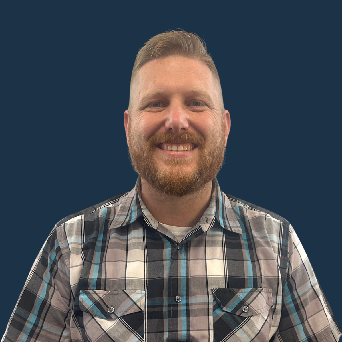 Smiling man with a beard in a blue plaid shirt against a dark blue background