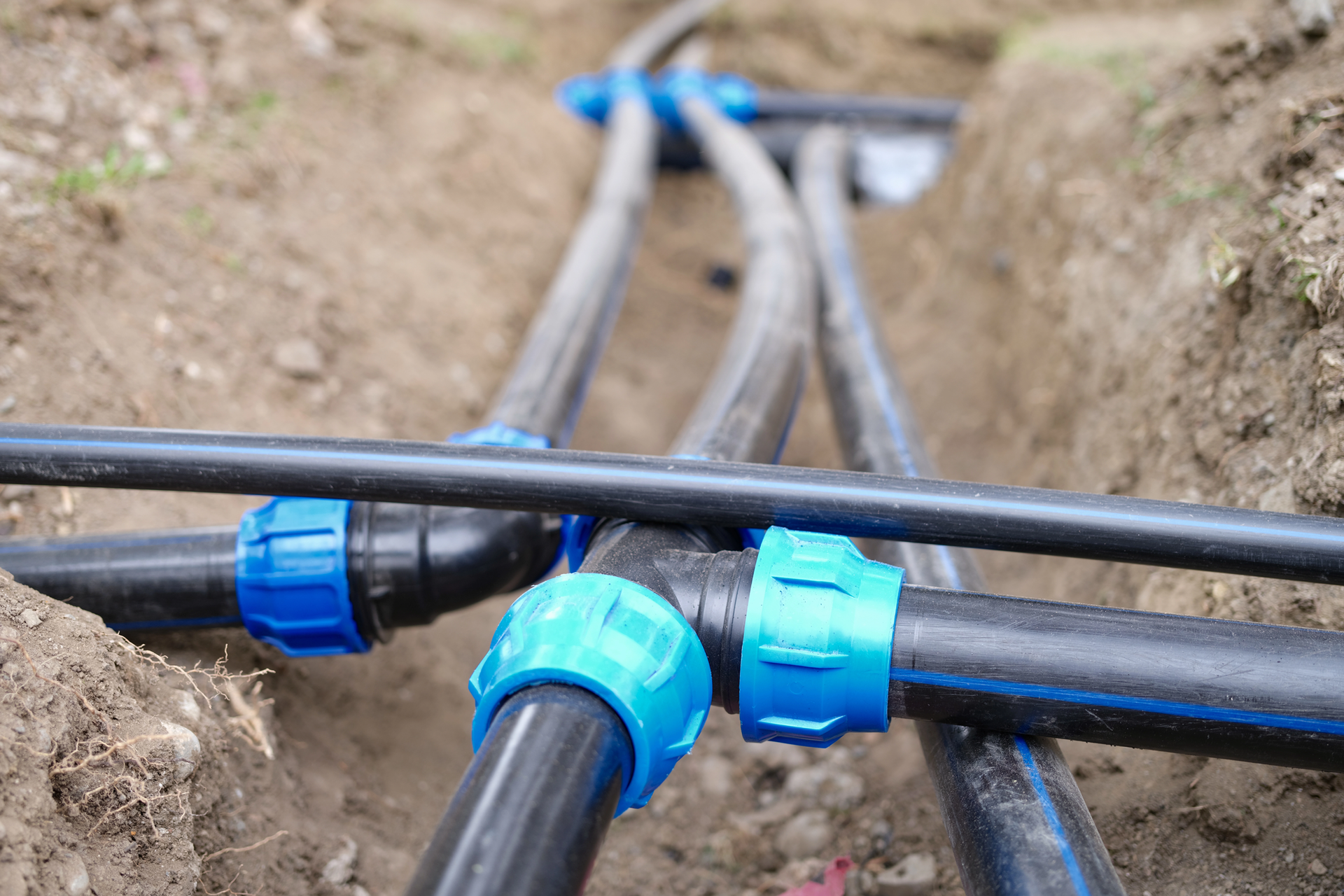 Black pipes joined with blue plastic couplings in an open dirt trench