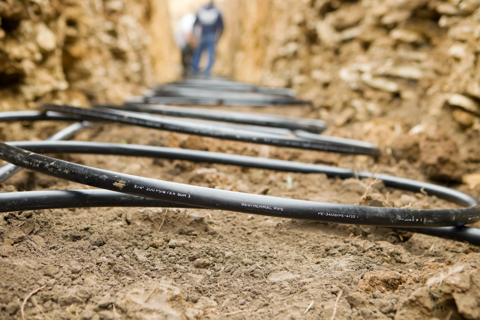 Black irrigation hoses laid in a dirt trench between rocky soil walls.