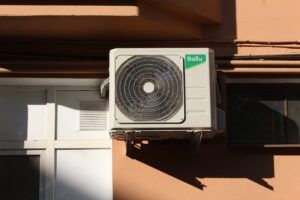 Wall-mounted air conditioner unit on a building exterior in sunlight.