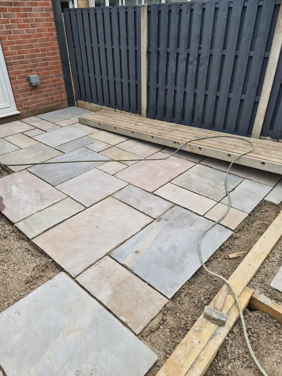 Newly installed natural stone patio beside a dark slatted fence in Cardiff