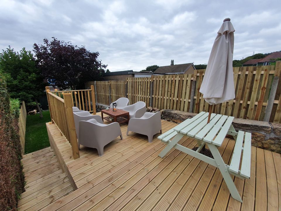 Raised timber deck with picket balustrade, garden furniture and a parasol in a Cardiff back garden
