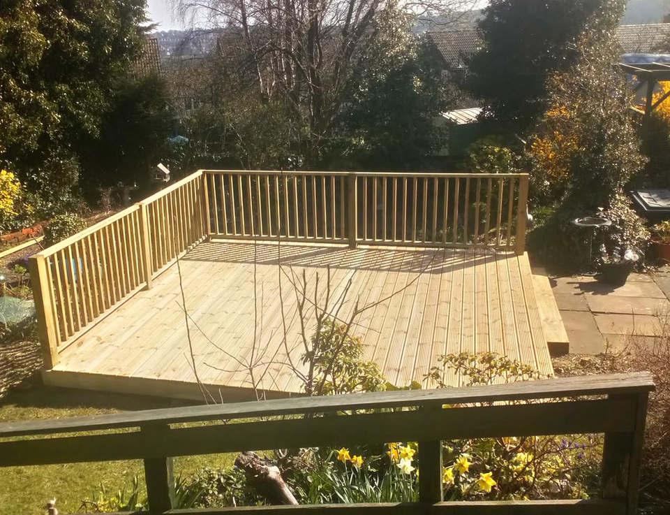Raised timber deck with a balustrade in a garden lit by low evening sun