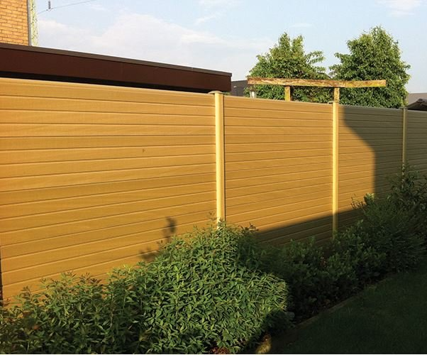 Natural beige eco composite fence panels in matching posts beside a shrub border