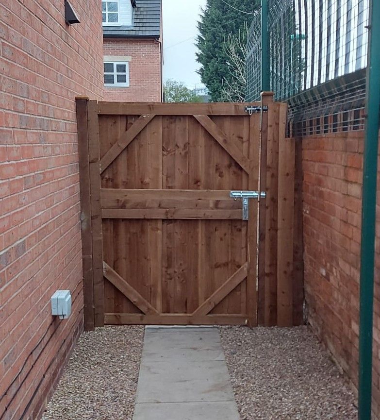 Timber side gate with a latch, fitted across a passage beside a brick house