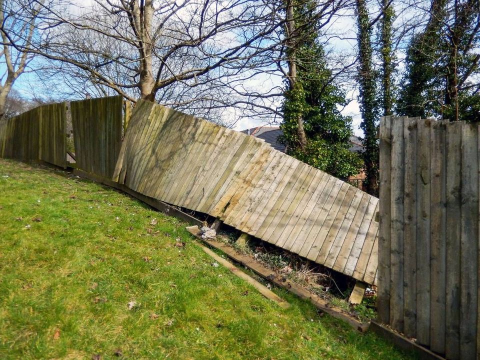 Timber fence panels leaning over at the bottom of a sloping lawn before repair
