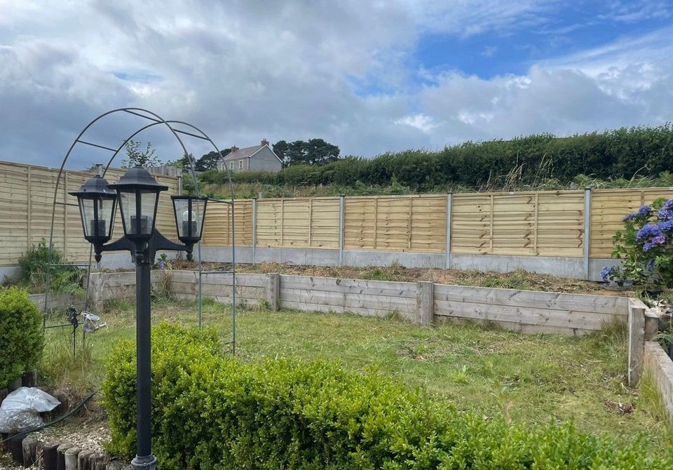 Finished lap panel fence on concrete posts behind a lawn with raised beds