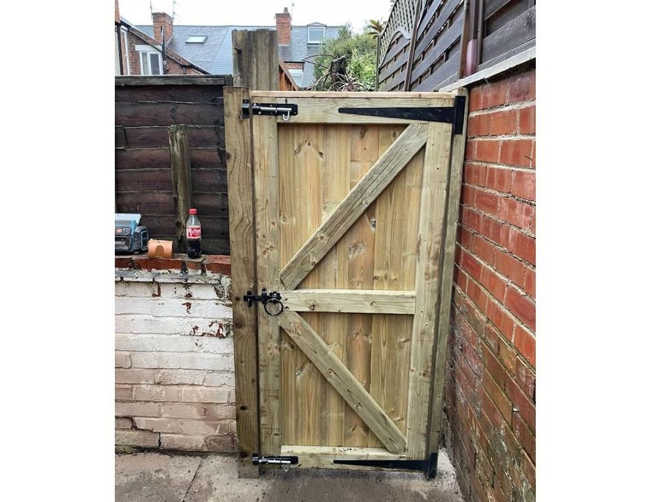 Pressure-treated ledged and braced gate with black hinges in a side passage