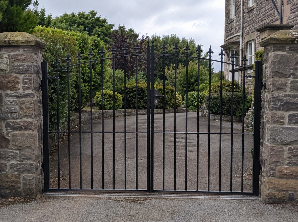 Black powder-coated metal driveway gates installed between stone pillars in Cardiff by J&Z Fencing