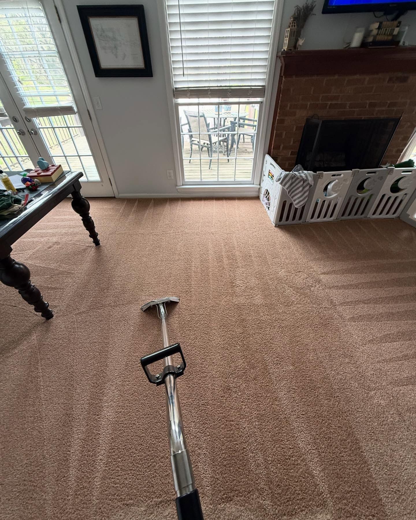 A person is using a carpet cleaner in a living room with light brown carpet and a fireplace.