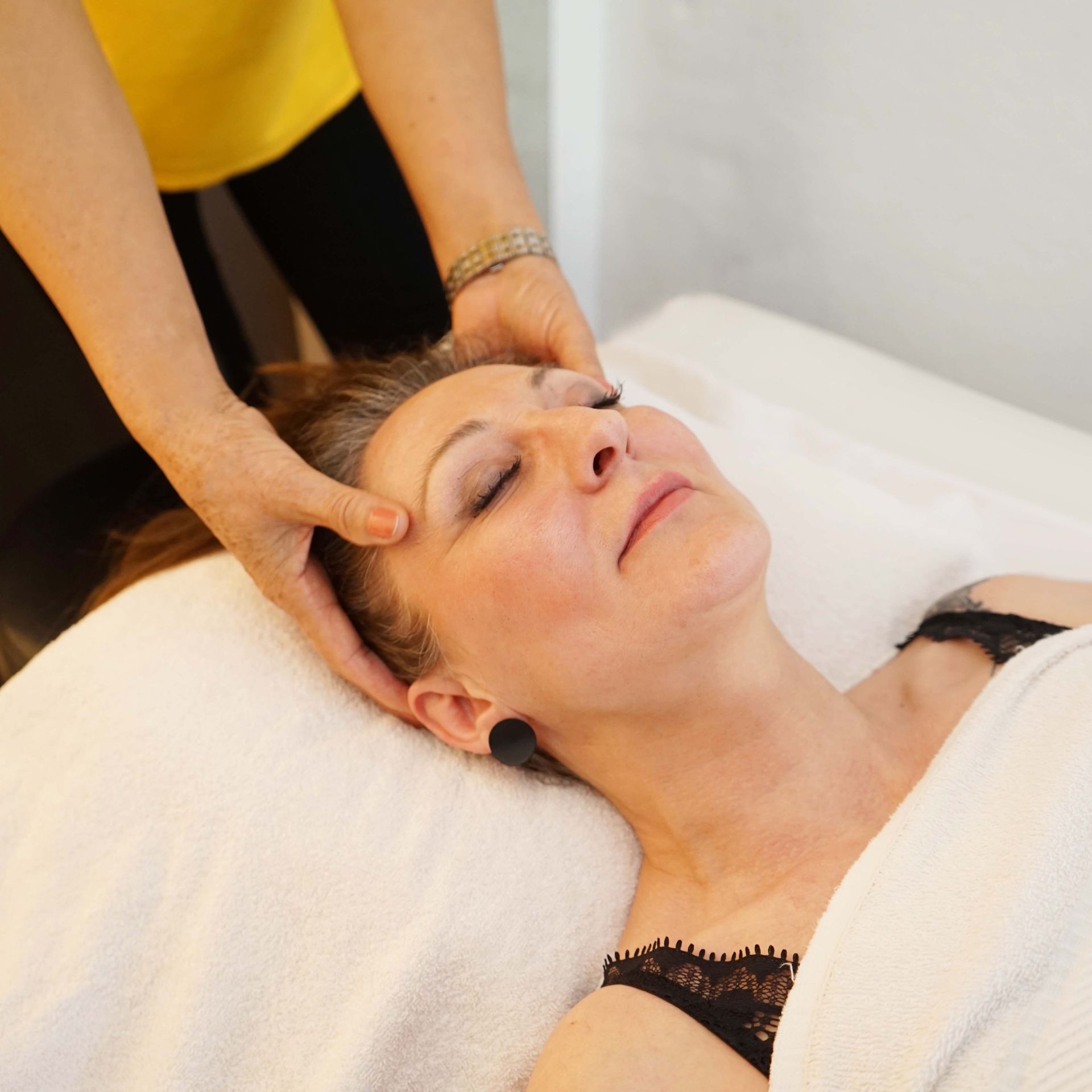 Eine Frau liegt auf einem Bett und bekommt eine Kopfmassage