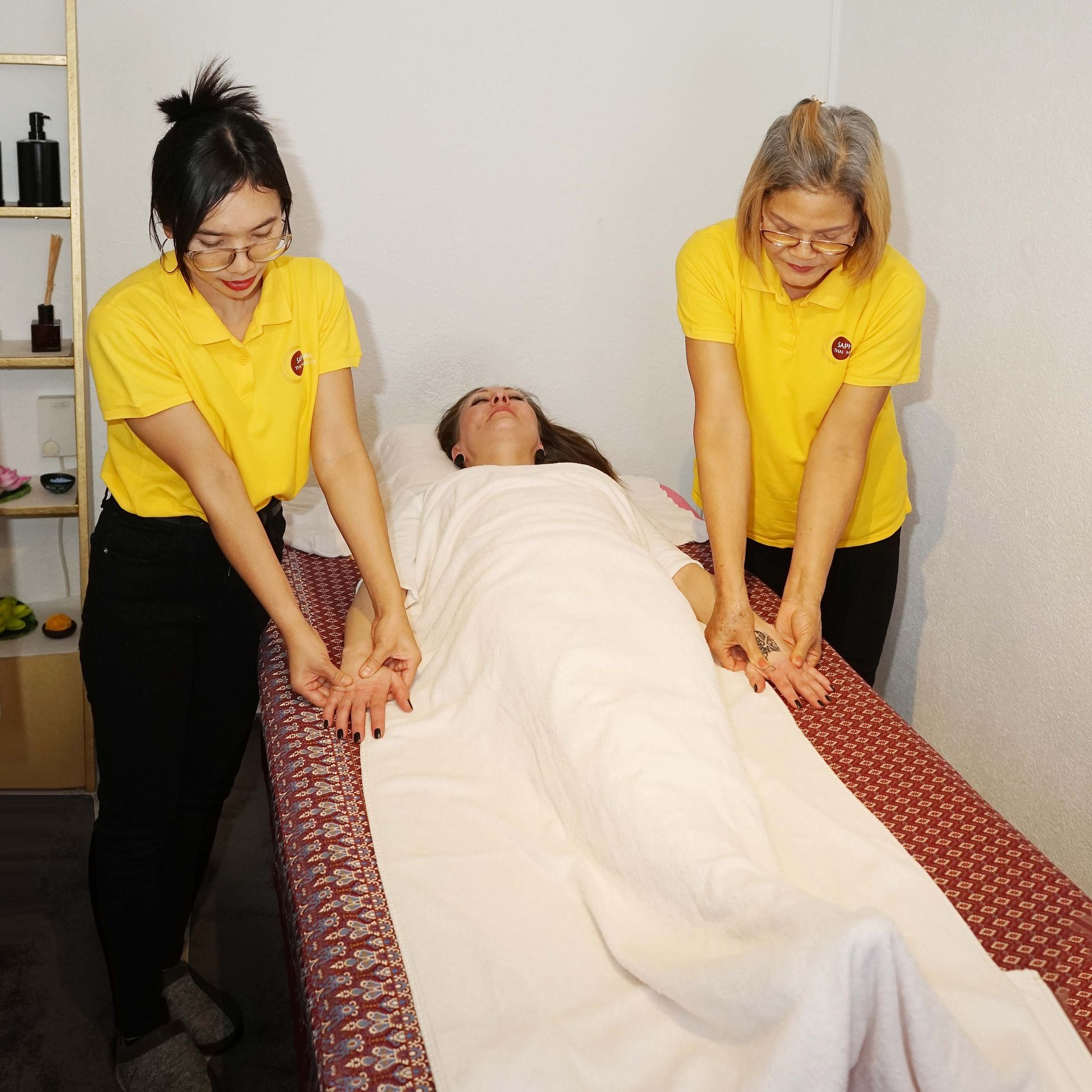 Zwei Frauen in gelben Hemden geben einer Frau eine Massage