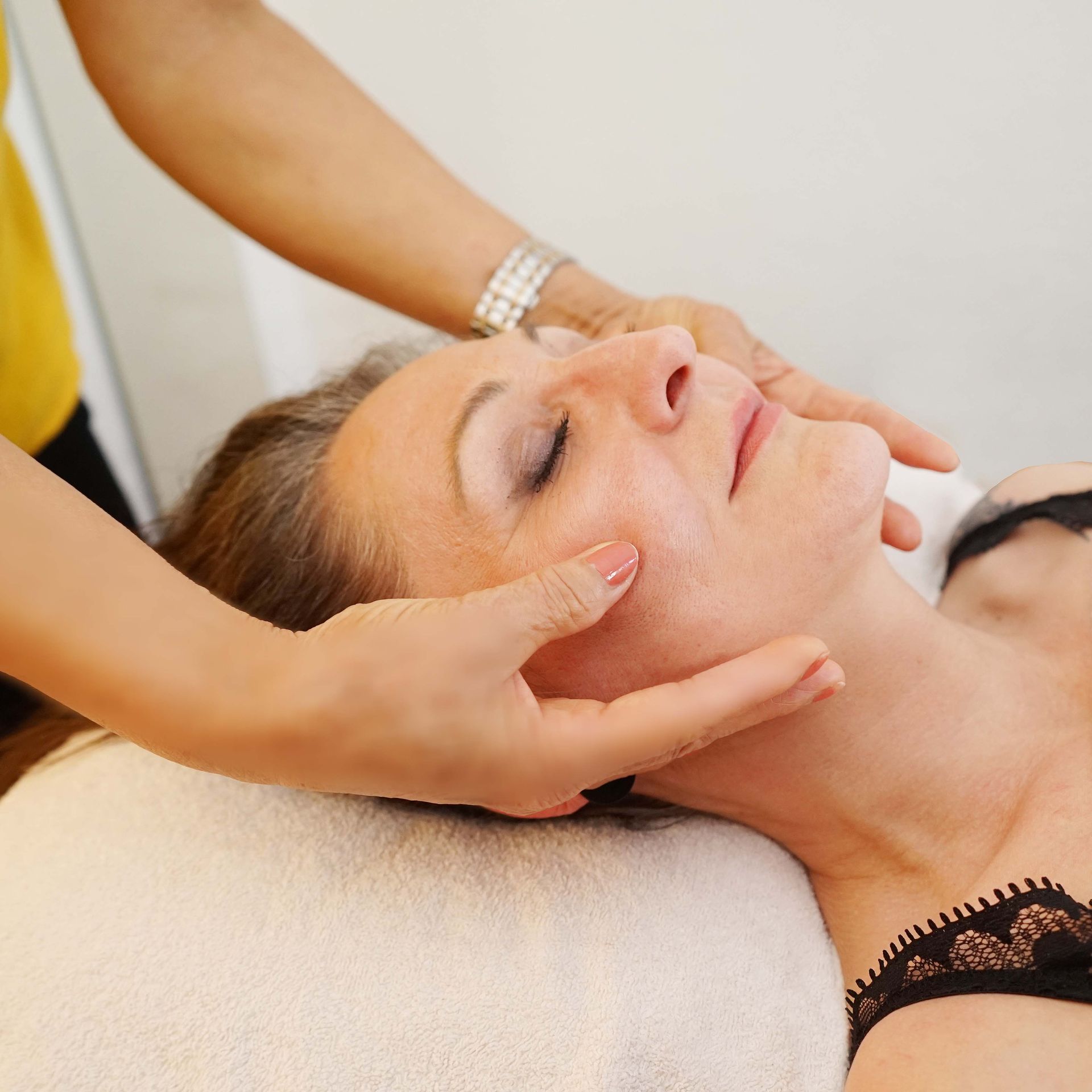 Eine Frau in einem schwarzen BH bekommt eine Gesichtsmassage