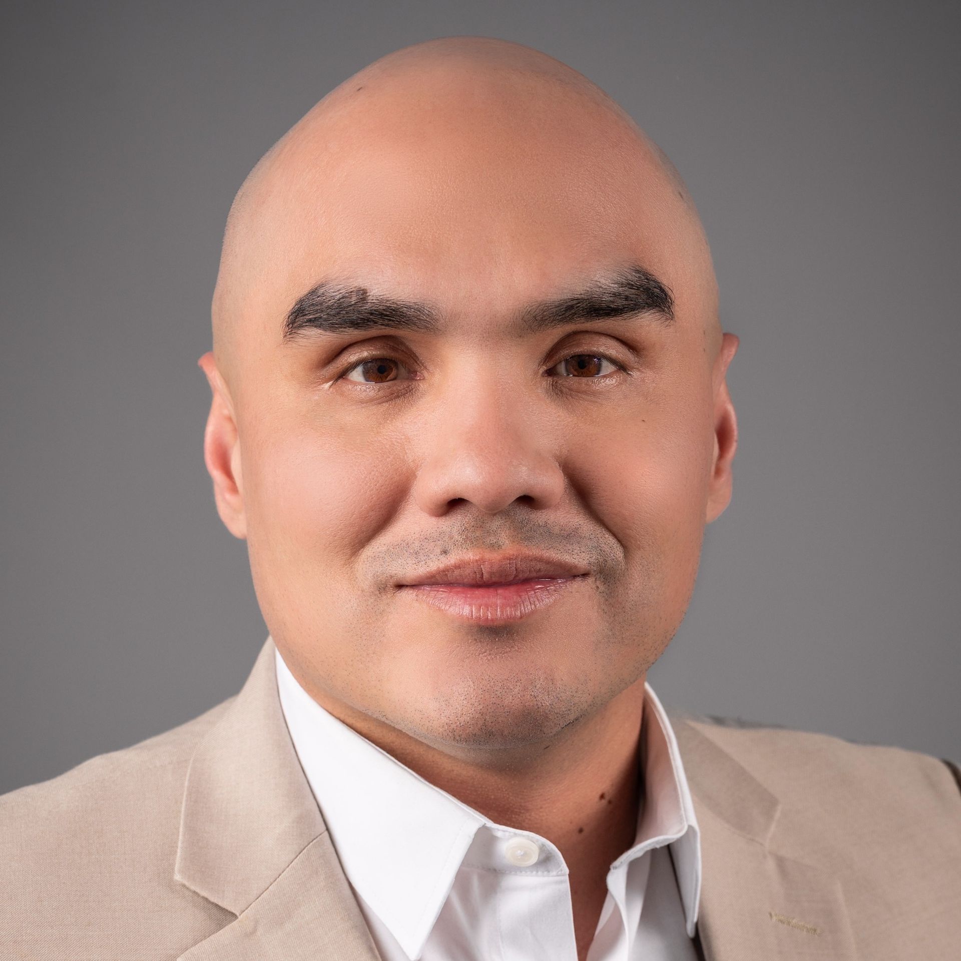 Studio portrait of a smiling bald man in a beige blazer and white shirt against a gray background