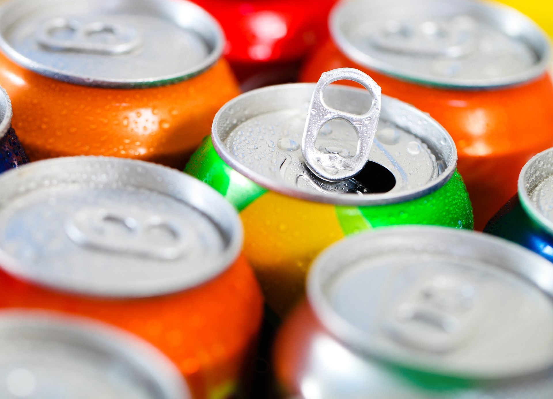 Primo piano di lattine di soda colorate; una è aperta con la linguetta rivolta verso l'alto, le altre sono sigillate.