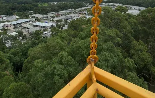 A Yellow Metal Structure With a Chain Hangs Against a Backdrop of a Green Forest — Summit Tree Services in Landsborough, QLD