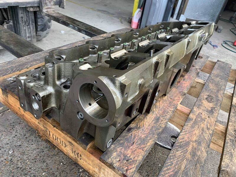 A cylinder head is sitting on top of a wooden pallet.