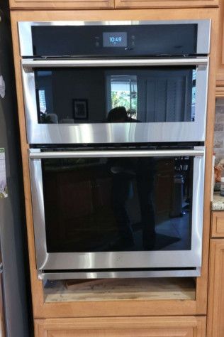 A stainless steel double oven is sitting on top of a wooden cabinet in a kitchen.