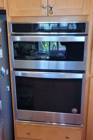 A stainless steel oven is sitting on top of a wooden cabinet in a kitchen.