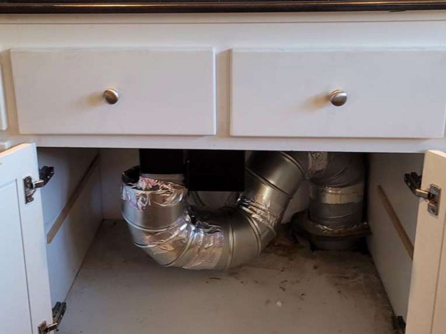 A metal pipe is coming out of the bottom of a cabinet.