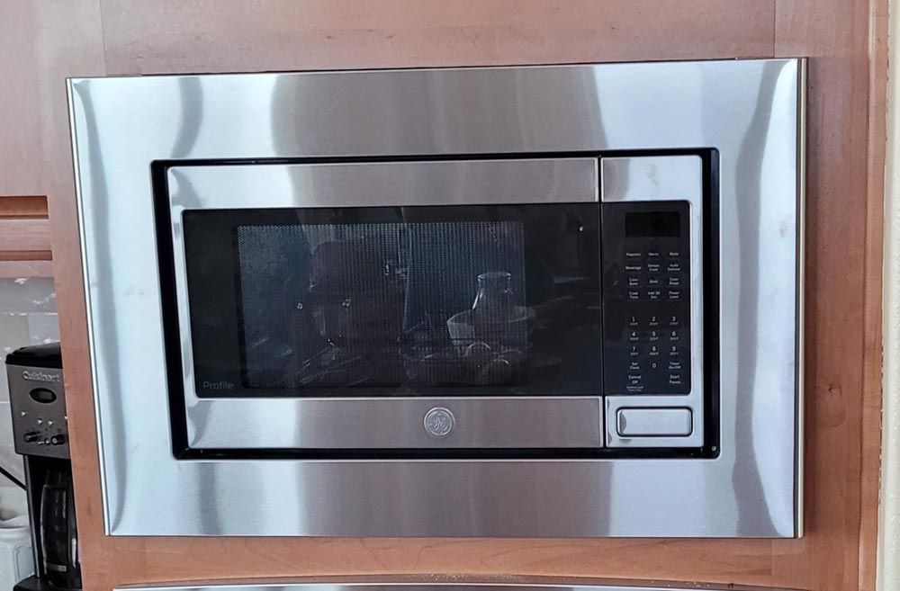 A stainless steel microwave oven is built into a wooden cabinet.