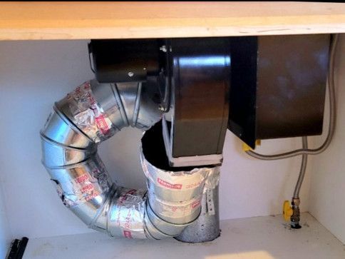 A metal pipe is connected to a fan in a cabinet.