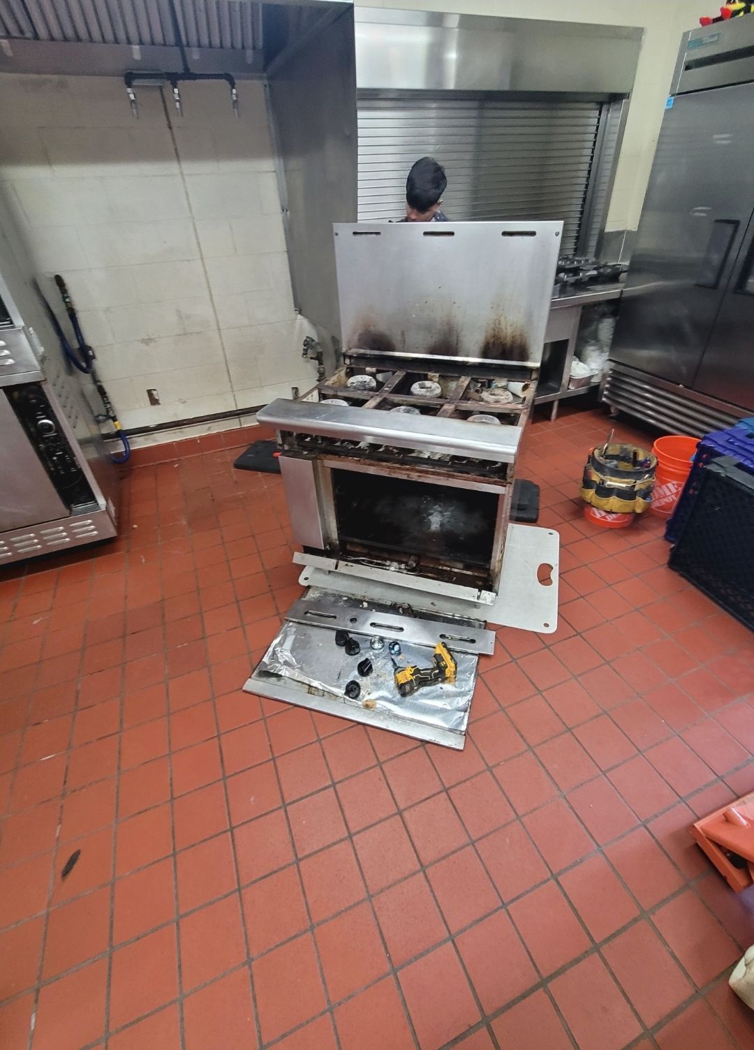A man is working on a stove in a kitchen.