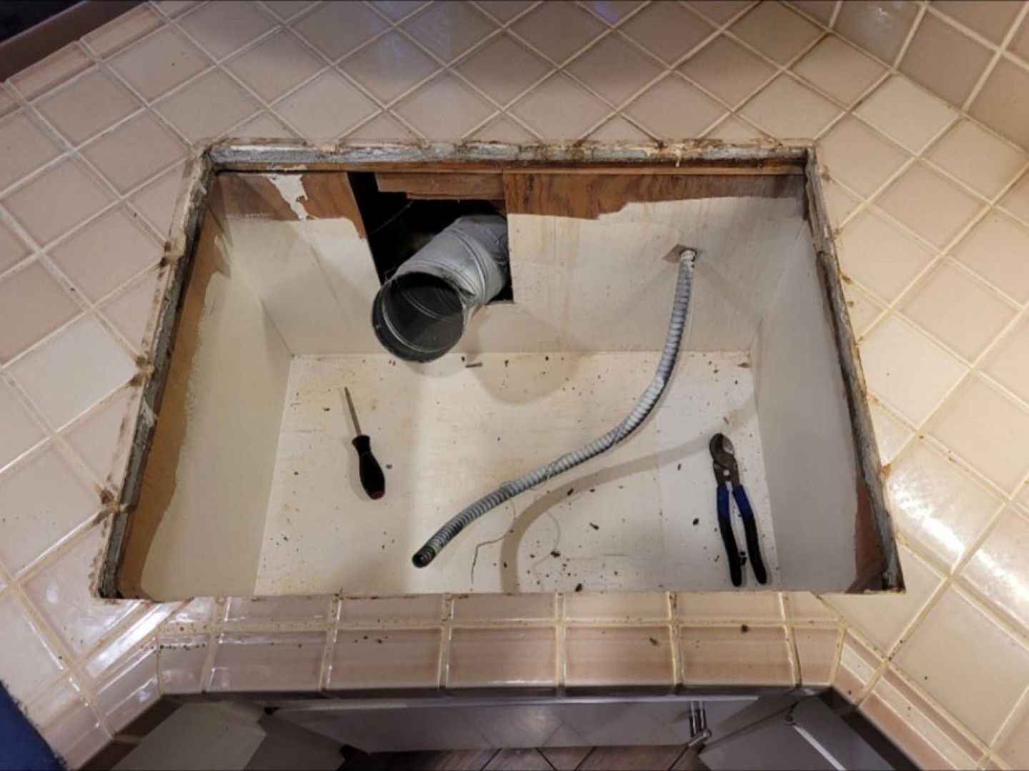 A hole in the floor of a kitchen with a hose coming out of it.