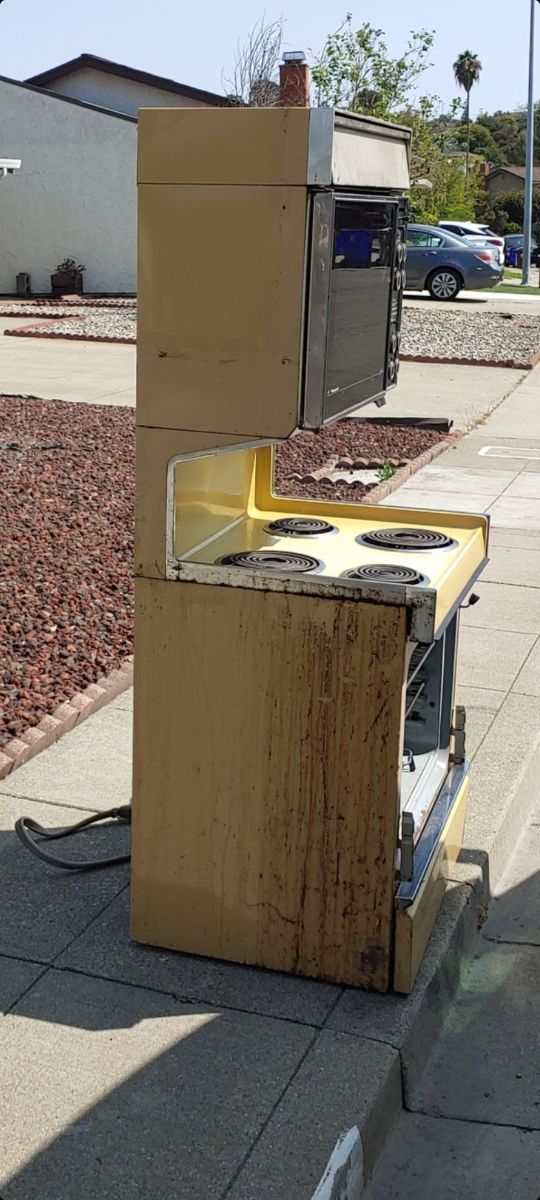 A yellow stove is sitting on the side of the road.