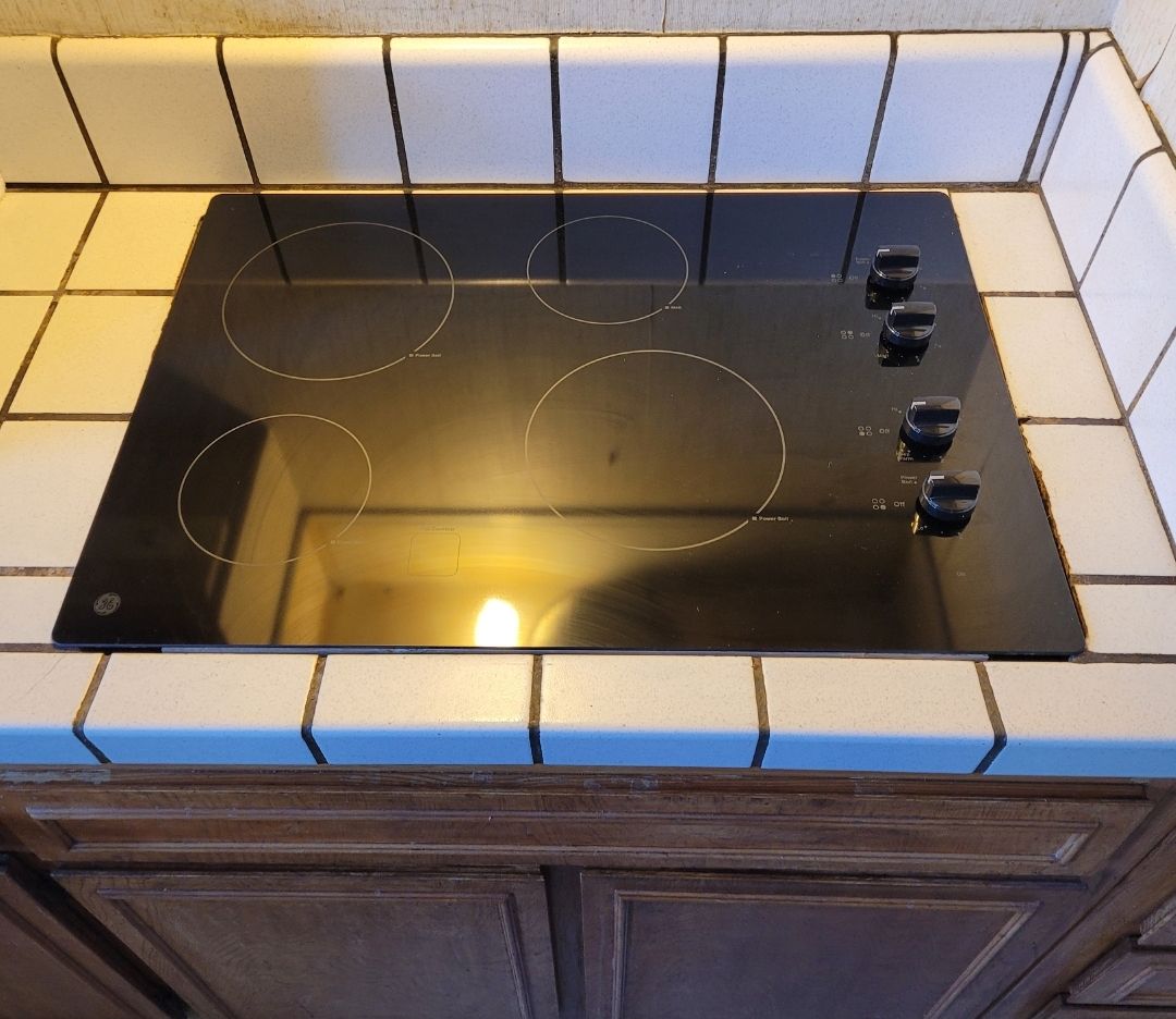 A black stove top sits on a tiled counter top
